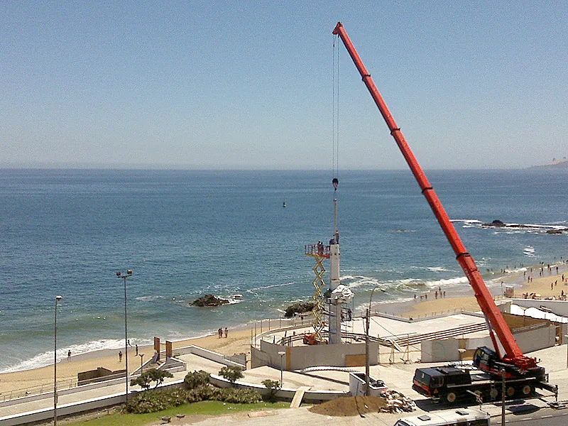 Grúa telescópica de Crane Service con la pluma extendida frente al mar, con un buque de fondo