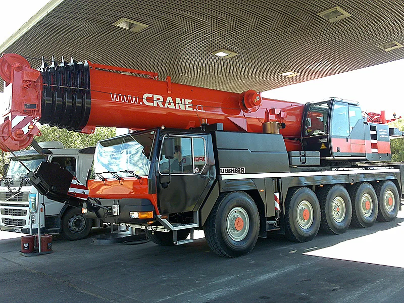 Grúa telescópica de 100 toneladas de Crane Service con la pluma recogida, rotulada www.crane.cl, bajo una techumbre industrial