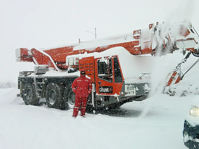 Operador con overol rojo junto a la grúa telescópica de 55 toneladas de Crane Service cubierta de nieve