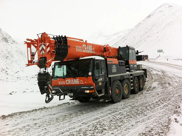 Grúa telescópica de 80 toneladas de Crane Service rotulada www.crane.cl, trasladándose por un camino de montaña con nieve