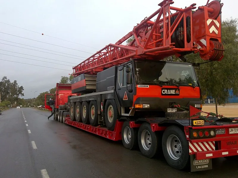 Cama baja de Crane Service transportando una grúa telescópica por camino rural