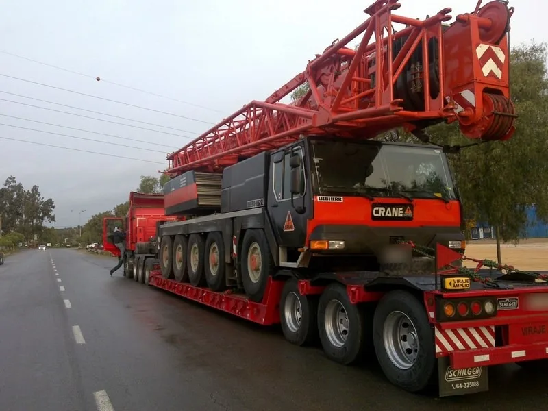 Cama baja de Crane Service trasladando por carretera una grúa telescópica con la pluma recogida
