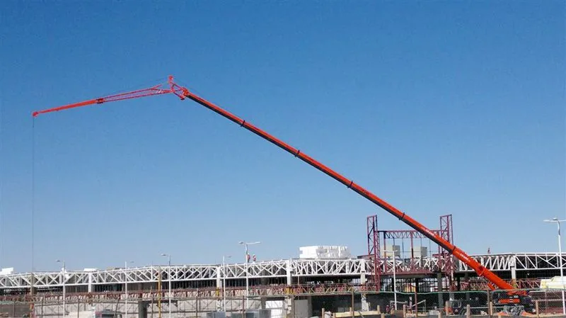 La grúa de 100 toneladas con la pluma desplegada en toda su extensión sobre una planta industrial, contra el cielo despejado