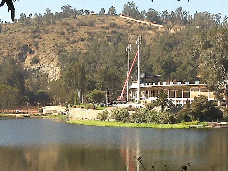 La grúa de 100 toneladas izando en una obra al borde de una laguna, con el cerro y la vegetación detrás