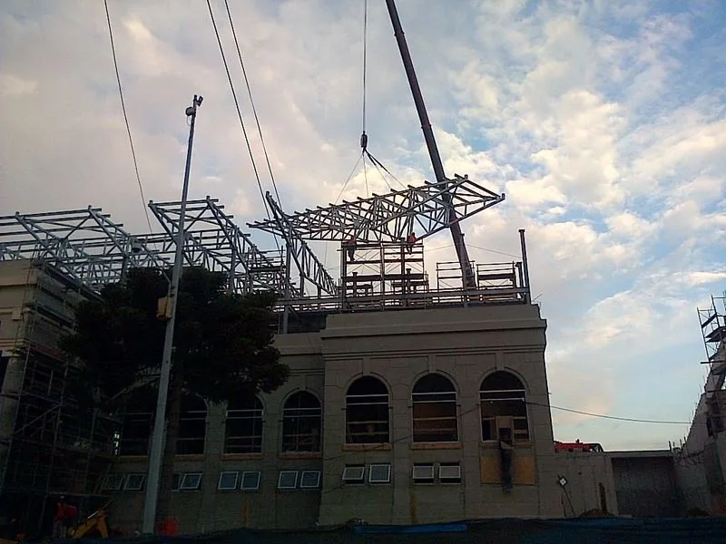 La grúa de 130 toneladas montando una estructura metálica de techumbre sobre un edificio patrimonial de fachada de ladrillo