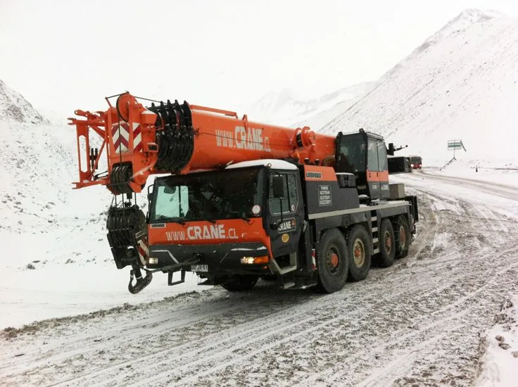 La grúa de 80 toneladas avanzando por un camino de cordillera cubierto de nieve, con el cerro nevado al costado