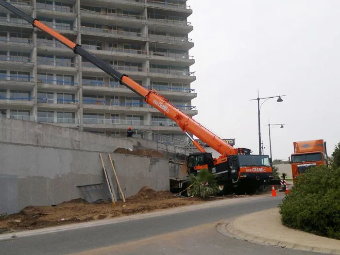 La grúa de 80 toneladas trabajando al pie de un edificio de varios pisos, apoyada sobre la calzada de una calle urbana
