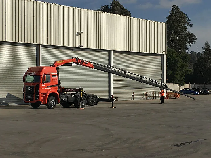 Tractocamión pluma de Crane Service con los estabilizadores desplegados junto a un galpón